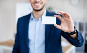 Cropped view of young Arab man showing empty business card with mockup for design at modern office.